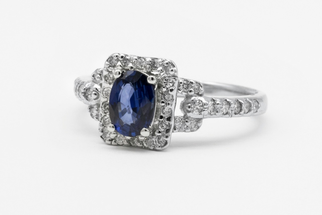 A white gold ring with an oval blue sapphire centerpiece on a white background